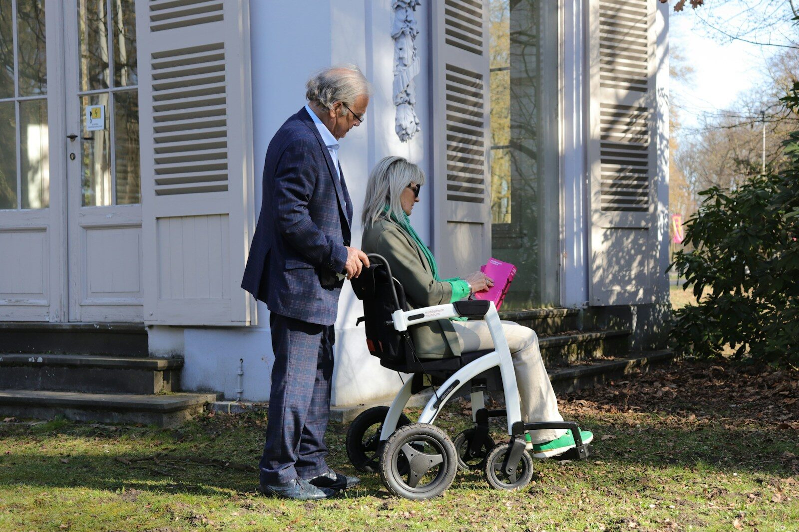 Man pushing woman in wheelchair outdoors near house